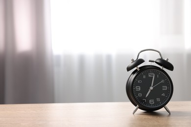 Photo of Black alarm clock on wooden table indoors, space for text