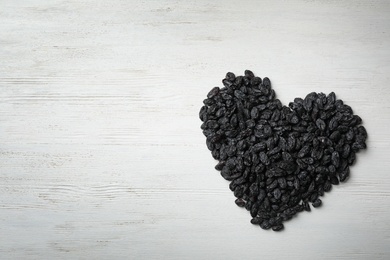 Photo of Heart shaped pile of raisins on wooden background, top view with space for text. Dried fruit as healthy snack