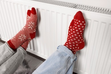 Photo of People warming feet near heating radiator indoors, closeup