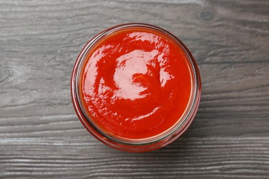 Photo of Tasty ketchup in jar on grey wooden table, top view. Tomato sauce