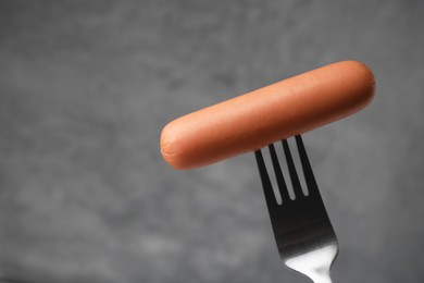 Photo of Delicious boiled sausage on fork against grey background, closeup. Space for text