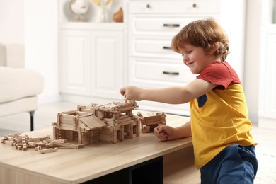 Photo of Cute little boy playing with wooden construction set at table in room. Child's toy