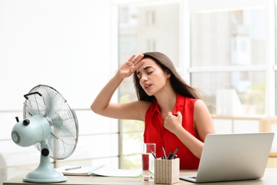Photo of Young woman with fan suffering from heat at workplace. Summer season