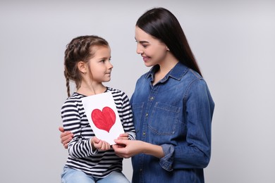 Photo of Happy woman with her daughter and handmade greeting card on light grey background. Mother's day celebration