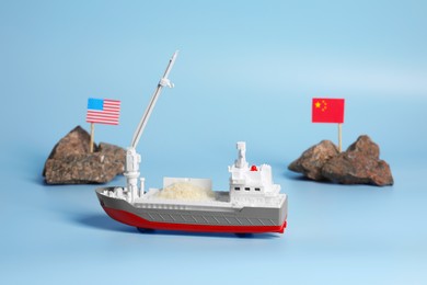 Photo of Toy cargo vessel, stones with American and Chinese flags on light blue background. Export concept