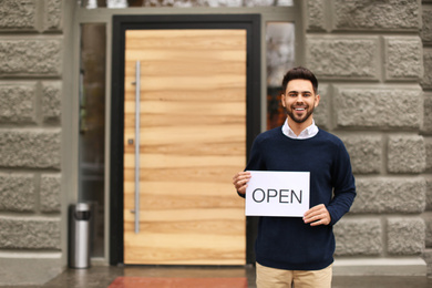 Photo of Young male business owner holding OPEN sign near his cafe. Space for text