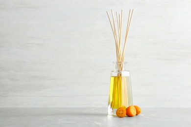 Photo of Aromatic reed freshener and kumquat on table against light background. Space for text