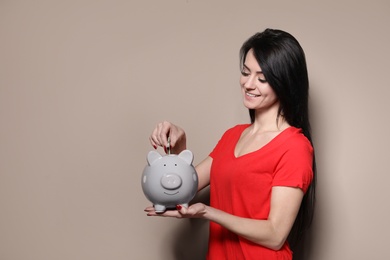 Photo of Woman putting money into piggy bank on color background. Space for text