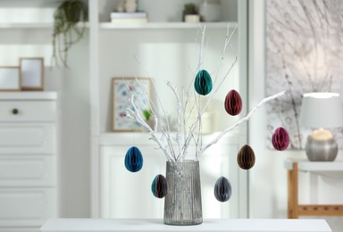 Photo of Branches with paper eggs in vase on white table at home, space for text. Beautiful Easter decor