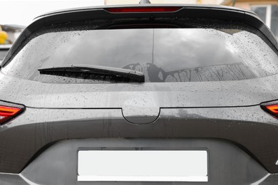 Photo of Car wiper cleaning water drops from rear windshield glass outdoors, closeup