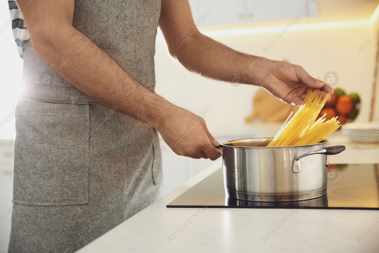 Photo of Man cooking pasta on stove in kitchen, closeup