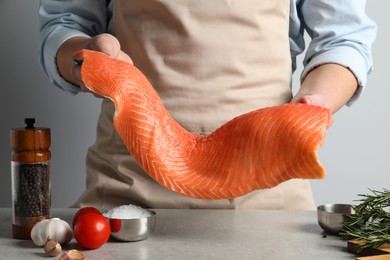 Photo of Man with raw salmon fillet at grey table, closeup