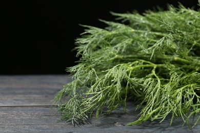 Photo of Fresh green dill on grey wooden table against black background, closeup. Space for text