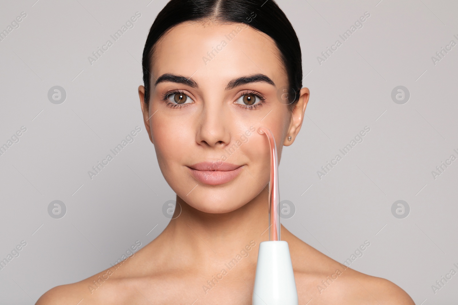 Photo of Woman using high frequency darsonval device on grey background