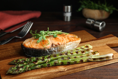 Photo of Tasty salmon steak served with asparagus and sprouts on wooden board