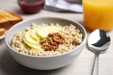 Photo of Tasty oatmeal porridge with walnuts and apple slices on white wooden table, closeup
