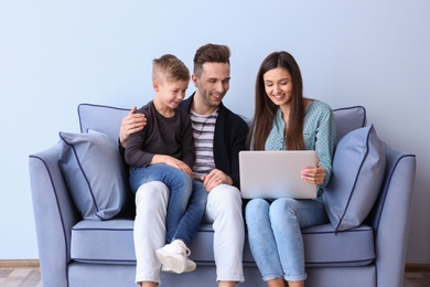 Photo of Happy family with laptop sitting on sofa, indoors
