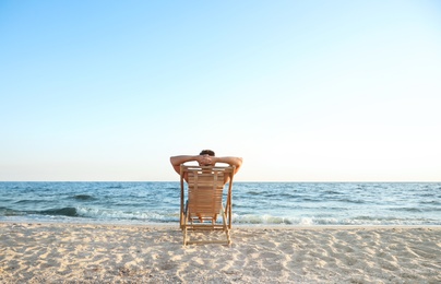 Photo of Young man relaxing in deck chair on beach near sea