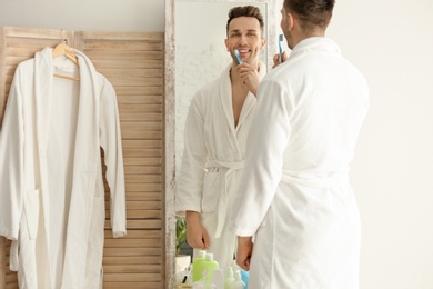 Photo of Young man looking in mirror while brushing teeth indoors