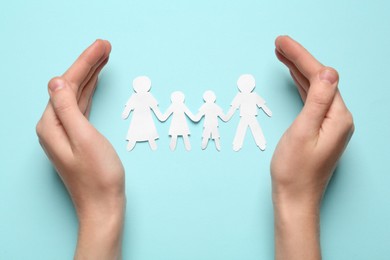 Photo of Woman protecting paper cutout of family on light blue background, top view