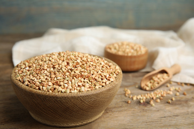 Photo of Uncooked green buckwheat grains in bowl on wooden table