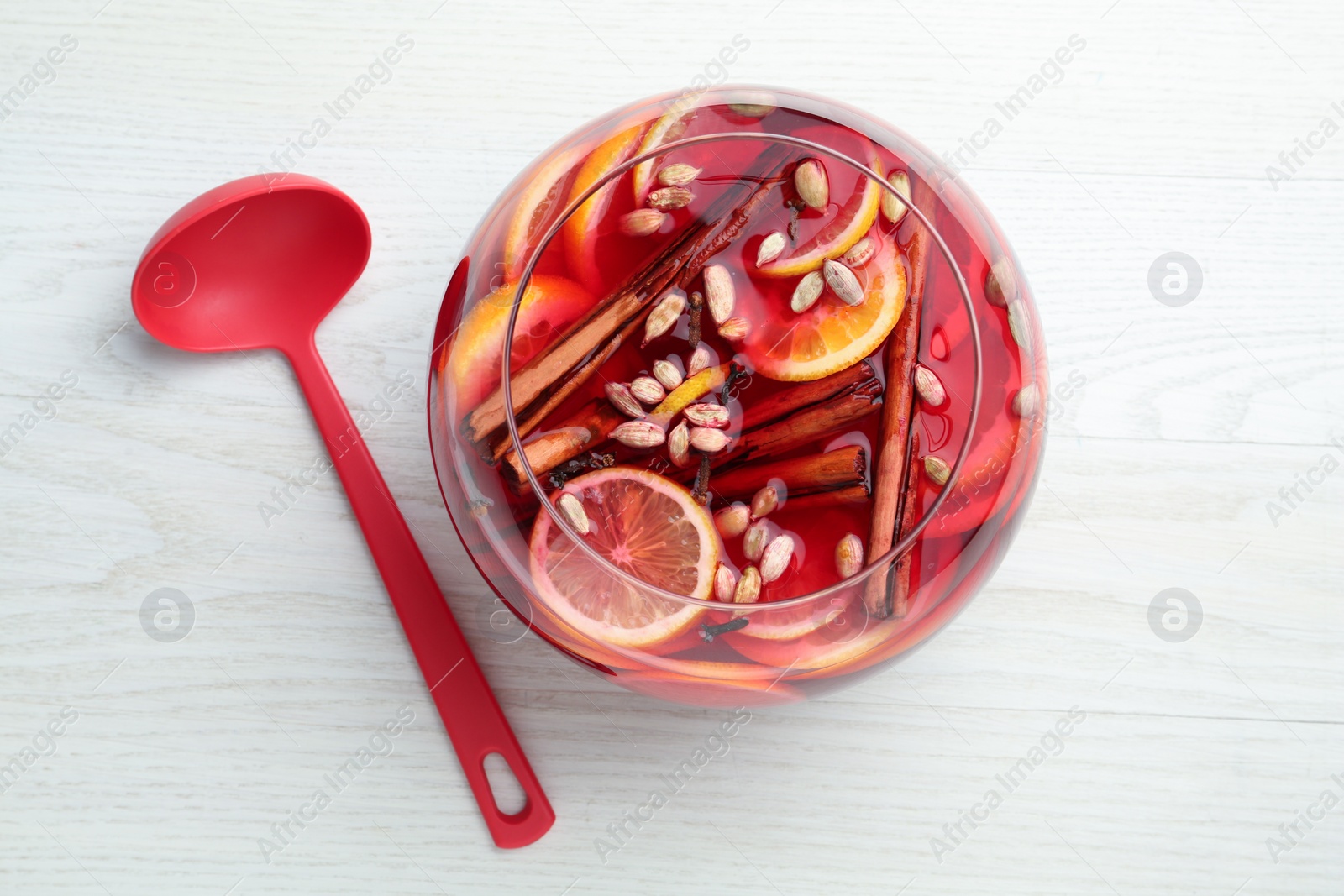 Photo of Glass bowl of delicious aromatic punch drink and ladle on white wooden table, flat lay