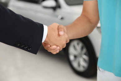Photo of Customer and salesman shaking hands in car salon