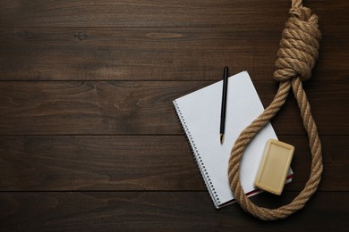 Photo of Rope noose, soap bar and blank notebook with pen on wooden table, flat lay. Space for text