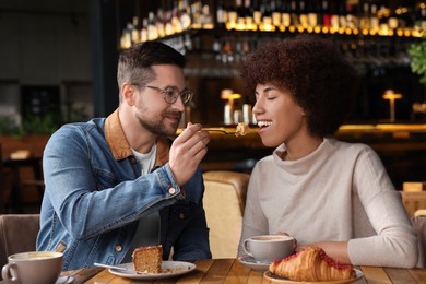 Photo of International dating. Beautiful woman feeding her boyfriend with cake in cafe