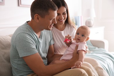 Photo of Happy couple holding their cute little baby with pacifier at home