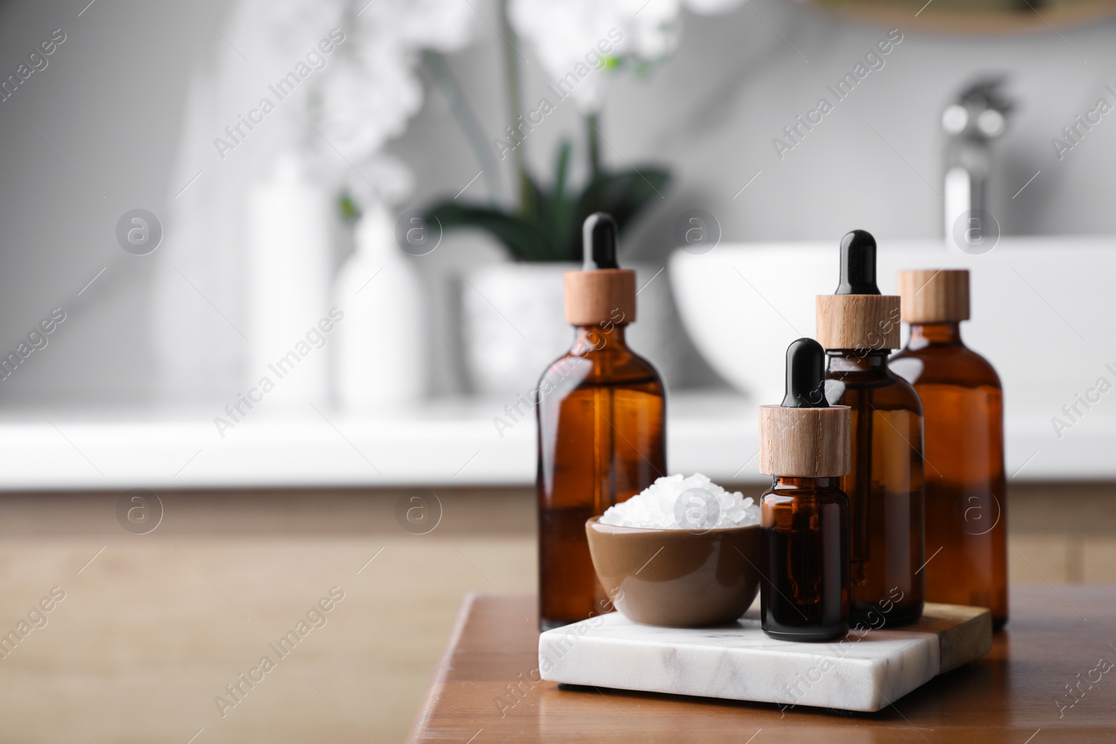 Photo of Essential oils and sea salt on wooden table in bathroom. Space for text