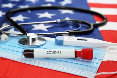 Photo of Test tube with blood, protective mask, stethoscope and thermometer on American flag. Coronavirus pandemic in USA