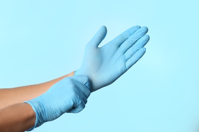 Photo of Person putting on latex gloves against light blue background, closeup