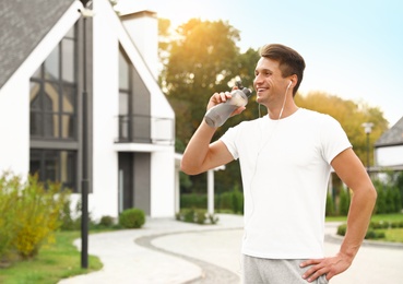 Photo of Young man with earphones drinking water after running on street. Healthy lifestyle