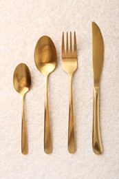 Photo of Stylish golden cutlery set on light textured table, flat lay