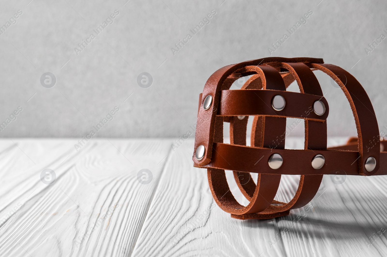 Brown leather dog muzzle on white wooden table, space for text Photo of Brown leather dog muzzle on white wooden table, space for text