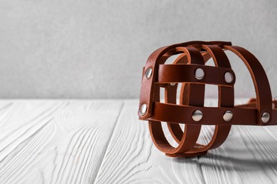 Photo of Brown leather dog muzzle on white wooden table, space for text