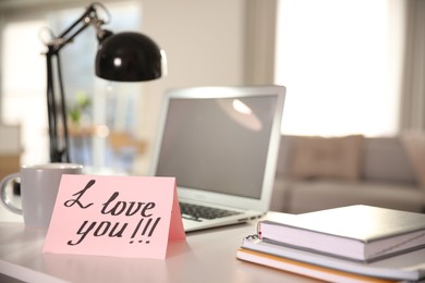 Photo of Note with handwritten text I Love You on workplace indoors. Romantic message