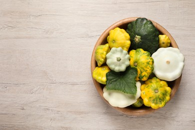 Photo of Fresh ripe pattypan squashes in bowl on light wooden table, top view. Space for text