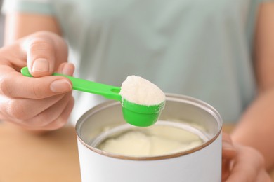 Photo of Woman with powdered infant formula at table, closeup. Preparing baby milk