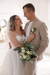 Photo of Happy groom with bouquet and bride indoors. Wedding day