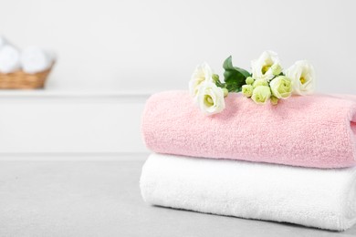Photo of Soft folded towels and eustoma flowers on white table, space for text