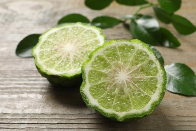 Photo of Halves of ripe bergamot fruit and green leaves on wooden table, closeup
