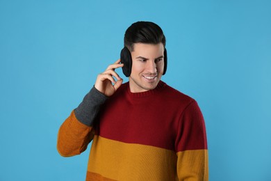 Man wearing stylish earmuffs on light blue background