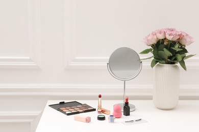 Photo of Mirror, cosmetic products and vase with pink roses on white dressing table in makeup room, space for text