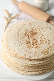 Photo of Tasty homemade tortillas, spikes and rolling pin on white wooden table