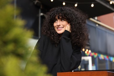 Photo of Happy young woman in stylish black sweater at wooden table outdoors
