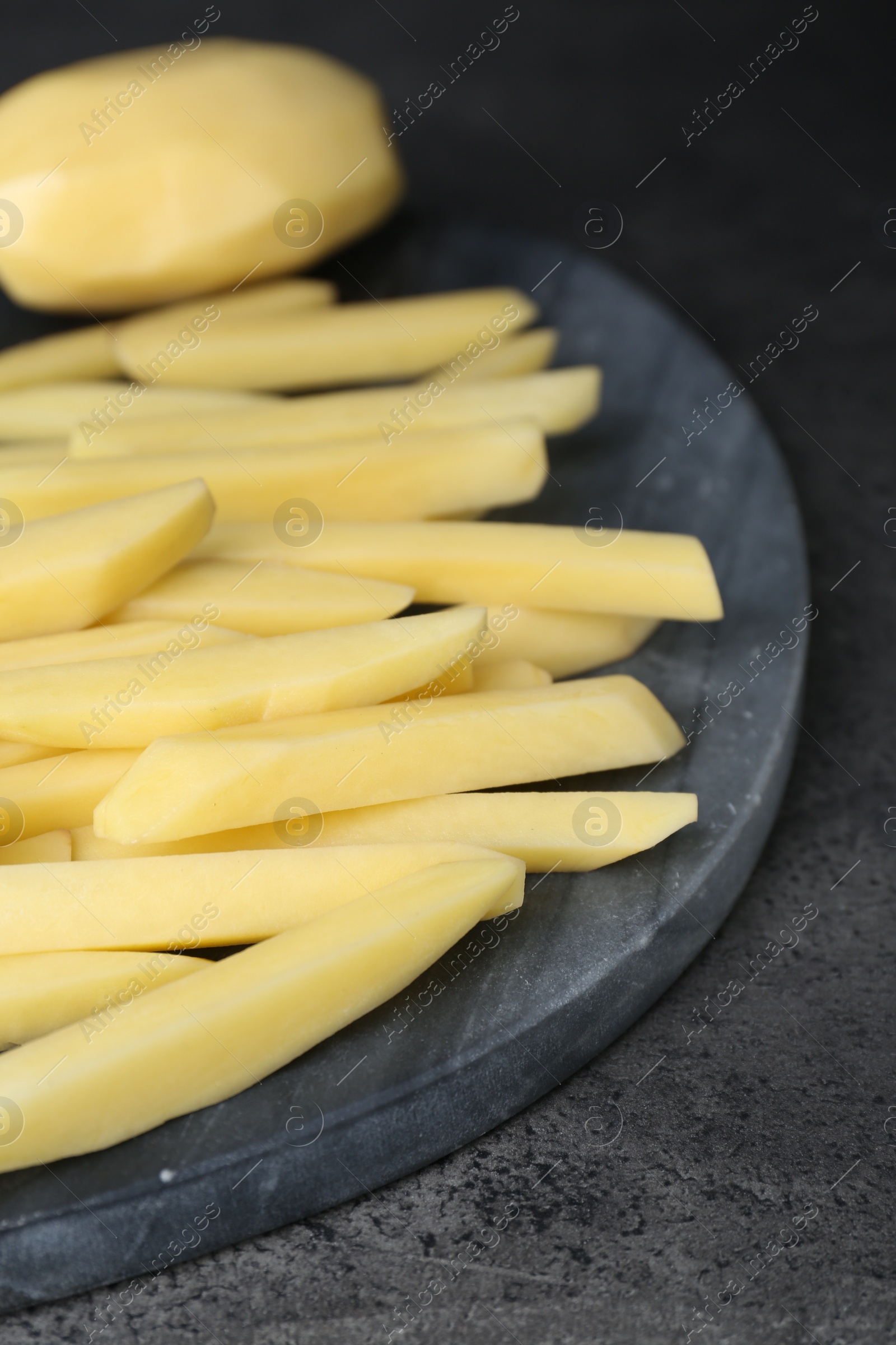 Photo of Whole and cut raw potatoes on grey table, closeup. Cooking delicious French fries