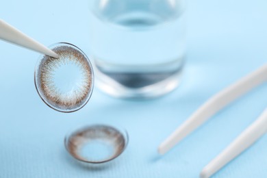 Tweezers with color contact lens on light blue background, closeup. Space for text