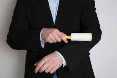 Photo of Man cleaning black jacket with lint roller on light grey background, closeup
